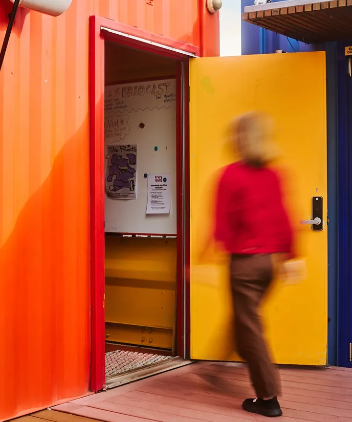 A presenter entering the orange FREOCAST studio through a yellow door