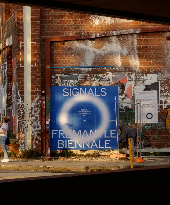 A blue Signals poster on a brick wall, seen through a Fremantle shop window