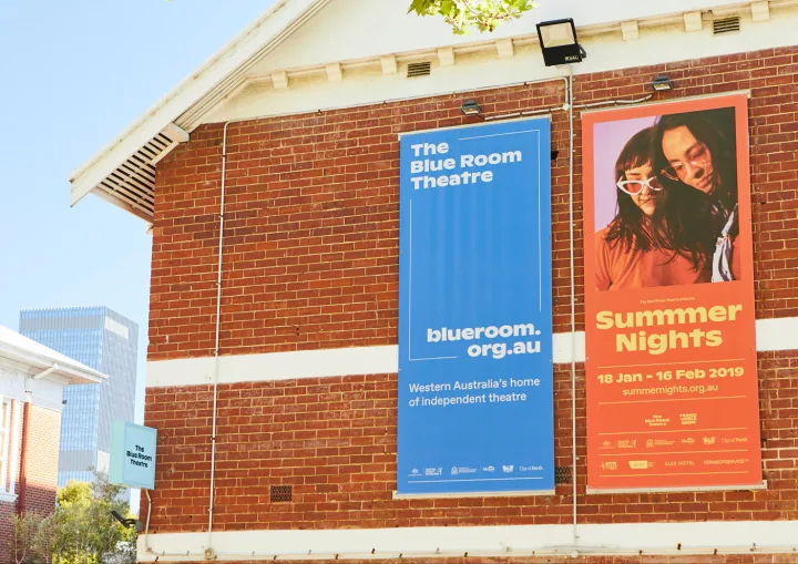 Blue theatre identity and orange Summer Nights banners on the brick theatre facade