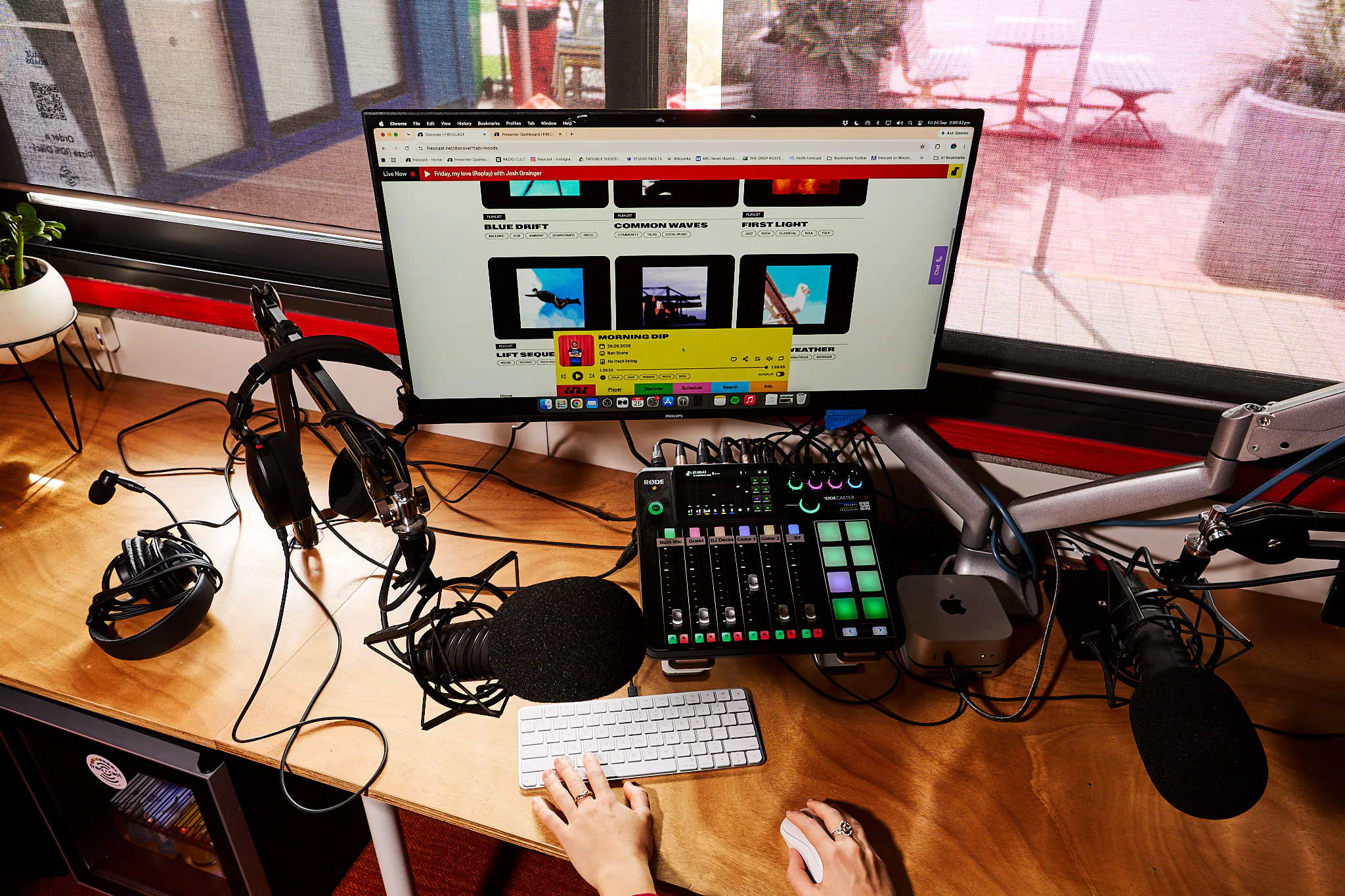 FREOCAST’s Discover page and yellow audio player on the studio computer, surrounded by microphones and a mixing desk