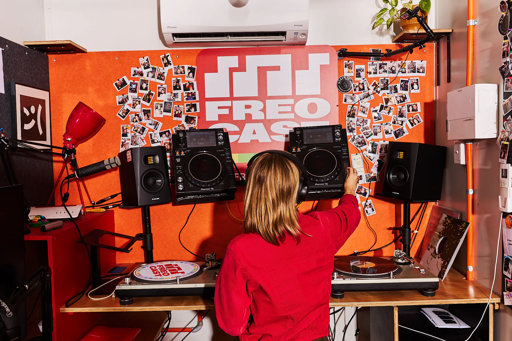 Presenter at the mixing desk in the red FREOCAST studio, beneath the station logo and community photographs