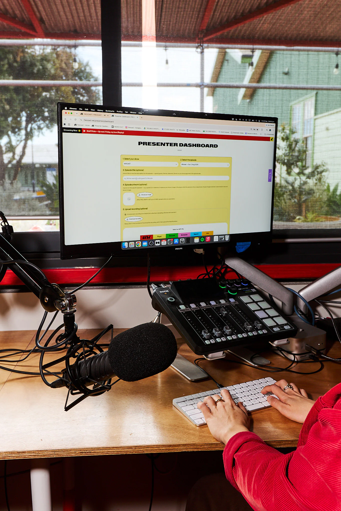 Presenter using the FREOCAST dashboard on a computer beside the studio mixing desk