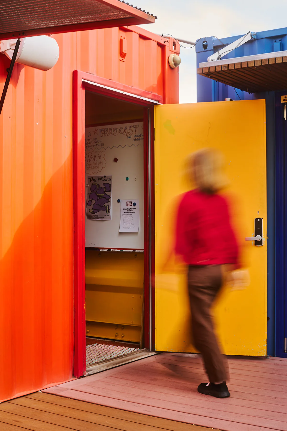 A person in red moving through FREOCAST’s orange studio entrance beside an open yellow door