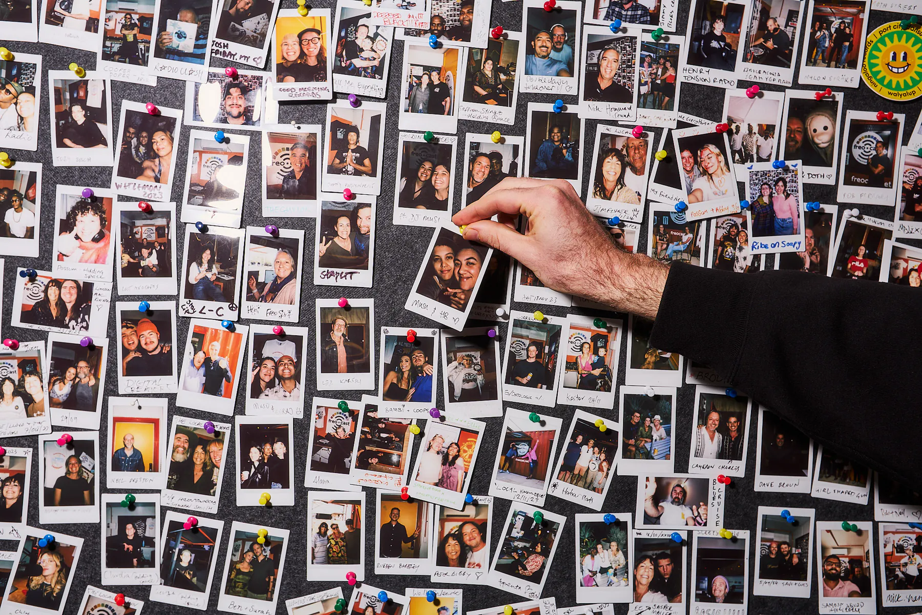 A hand adding an instant photograph to FREOCAST’s wall of presenter and community portraits