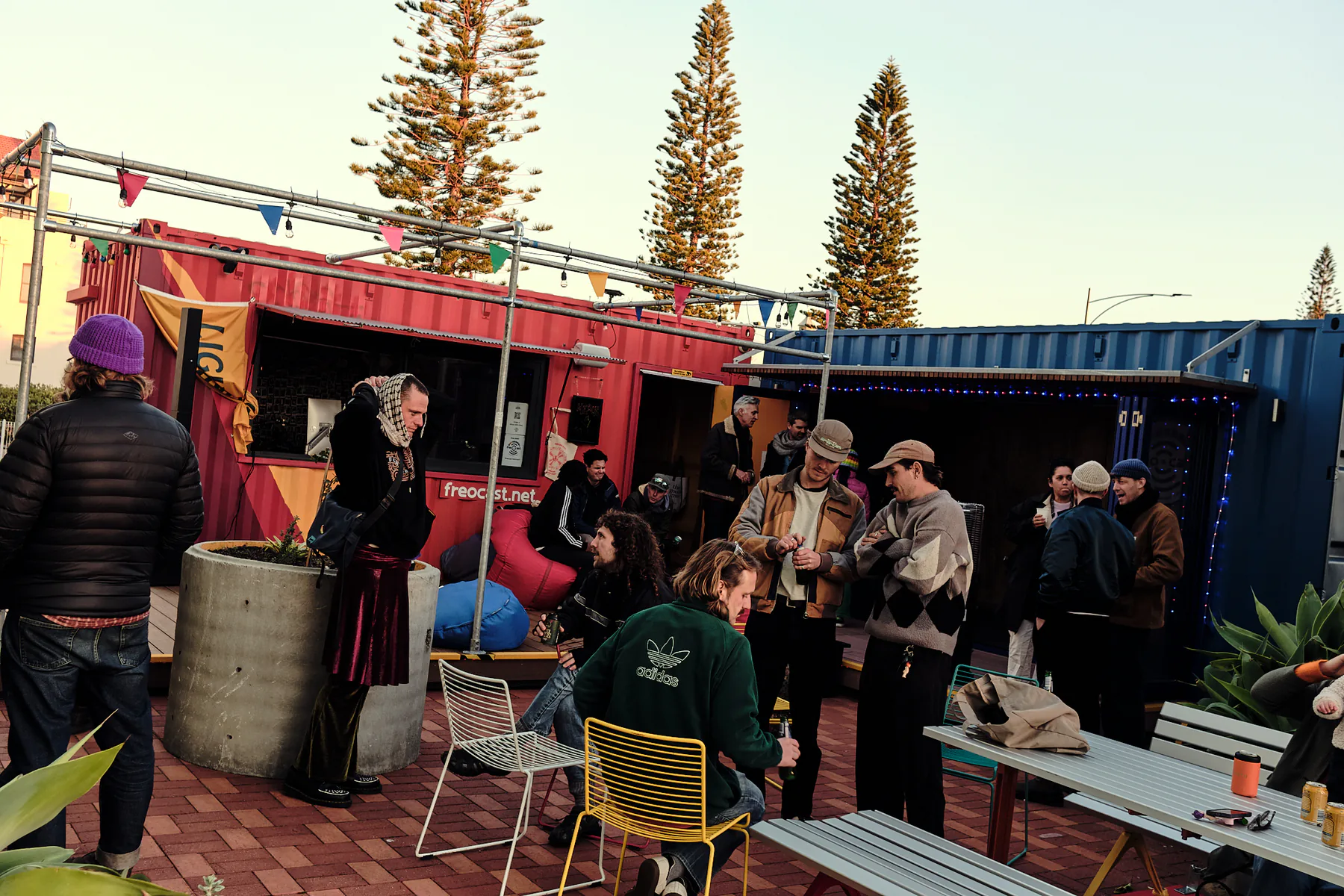 People gathered around tables in the courtyard between FREOCAST’s red and blue container studios