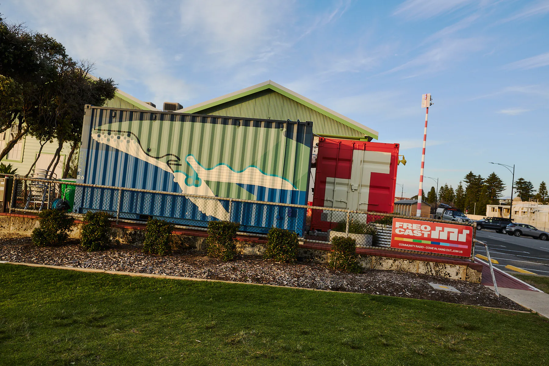 FREOCAST’s blue and red shipping-container studios viewed from the street, with port-crane graphics and station signage