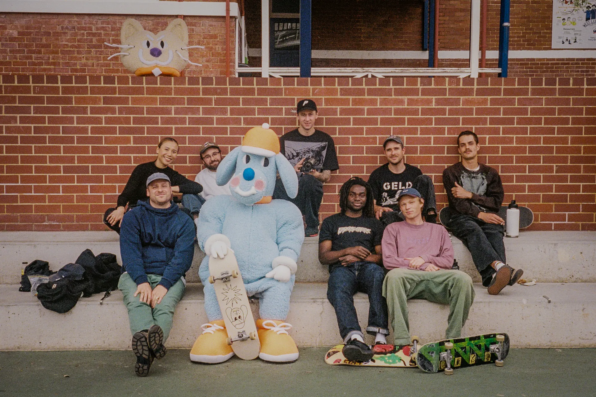 The blue Sports Dreams mascot sitting with skateboarders beside the basketball court